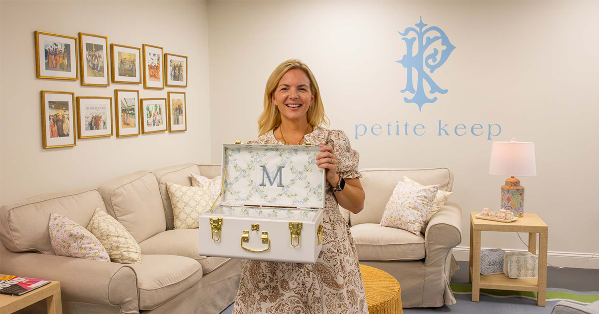 Smiling woman holding an open white keepsake case monogrammed "M" in a Petite Keep showroom