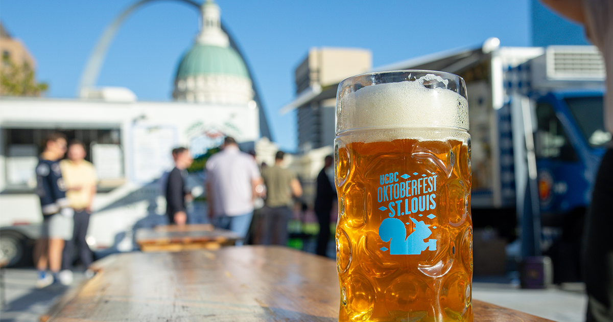 Beer stein labeled "UCBC Oktoberfest St. Louis" with the Gateway Arch and crowd in the background
