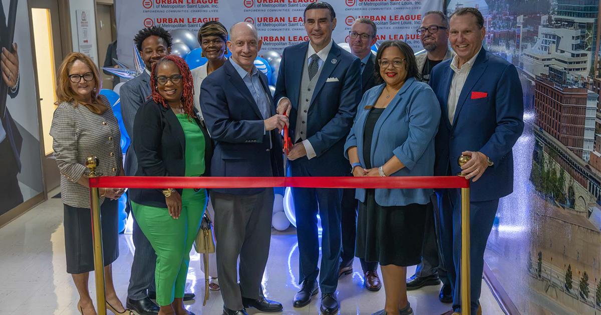 Group at a ribbon-cutting ceremony for the Urban League of Metropolitan Saint Louis, with two men cutting a red ribbon